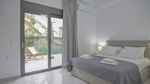 A modern bedroom with a large bed, a sliding glass door to a balcony, and a small bedside table with a lamp. - Moka Apartments (Chania)