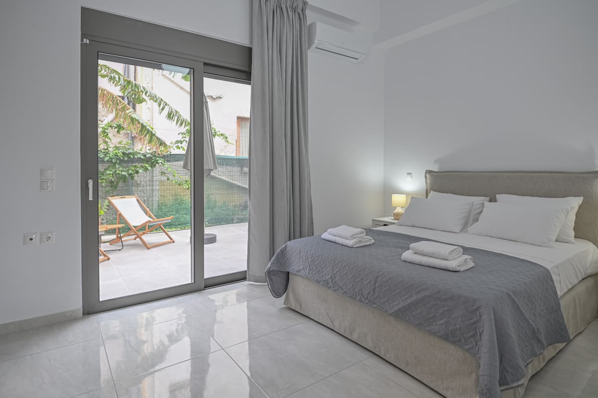 A modern bedroom with a large bed, a sliding glass door to a balcony, and a small bedside table with a lamp.