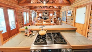 A log cabin interior with a kitchen area featuring a stove, a dining table, and chairs. - Rainbow Lodge - exceptional lakeside log home (Mazama)