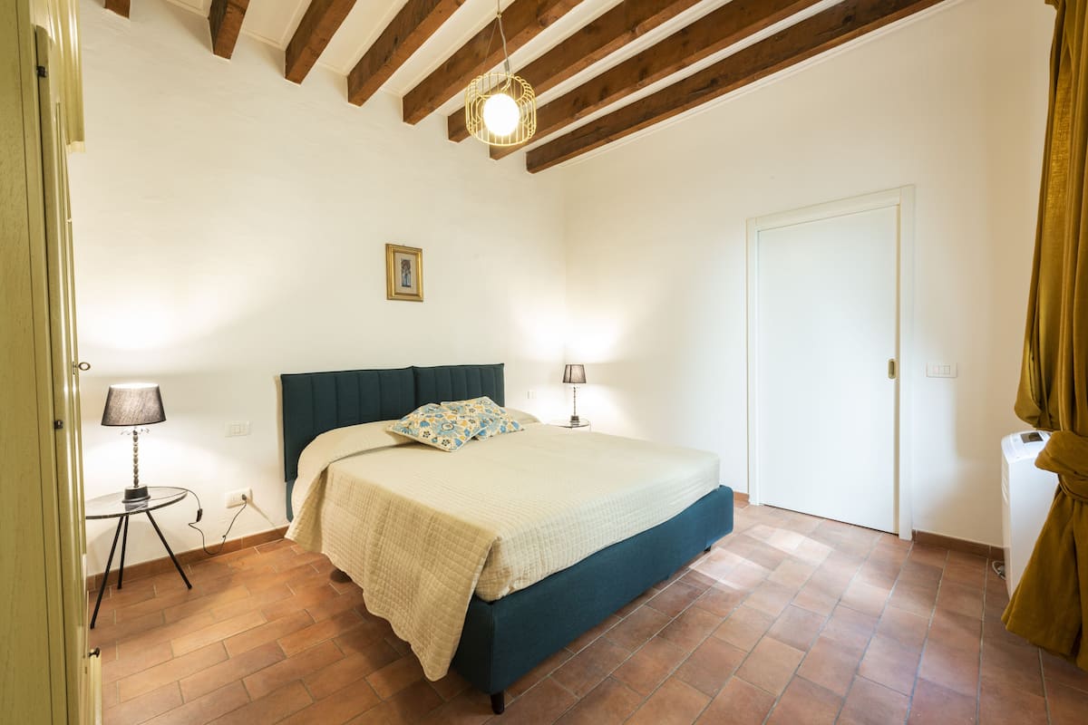 A bedroom with a bed, two bedside lamps, a picture on the wall, and a door.