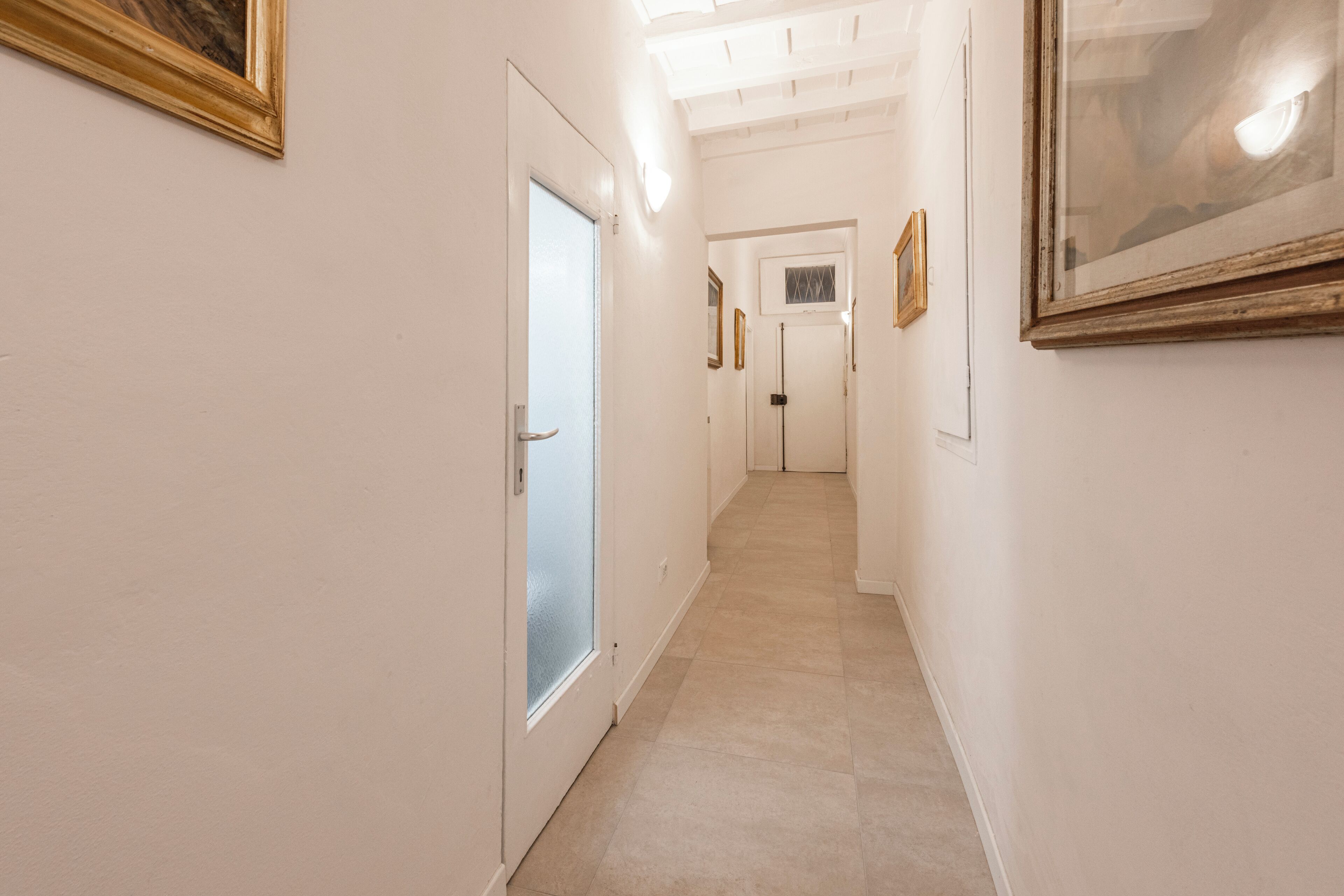 A hallway with a door, framed pictures, and a light fixture.