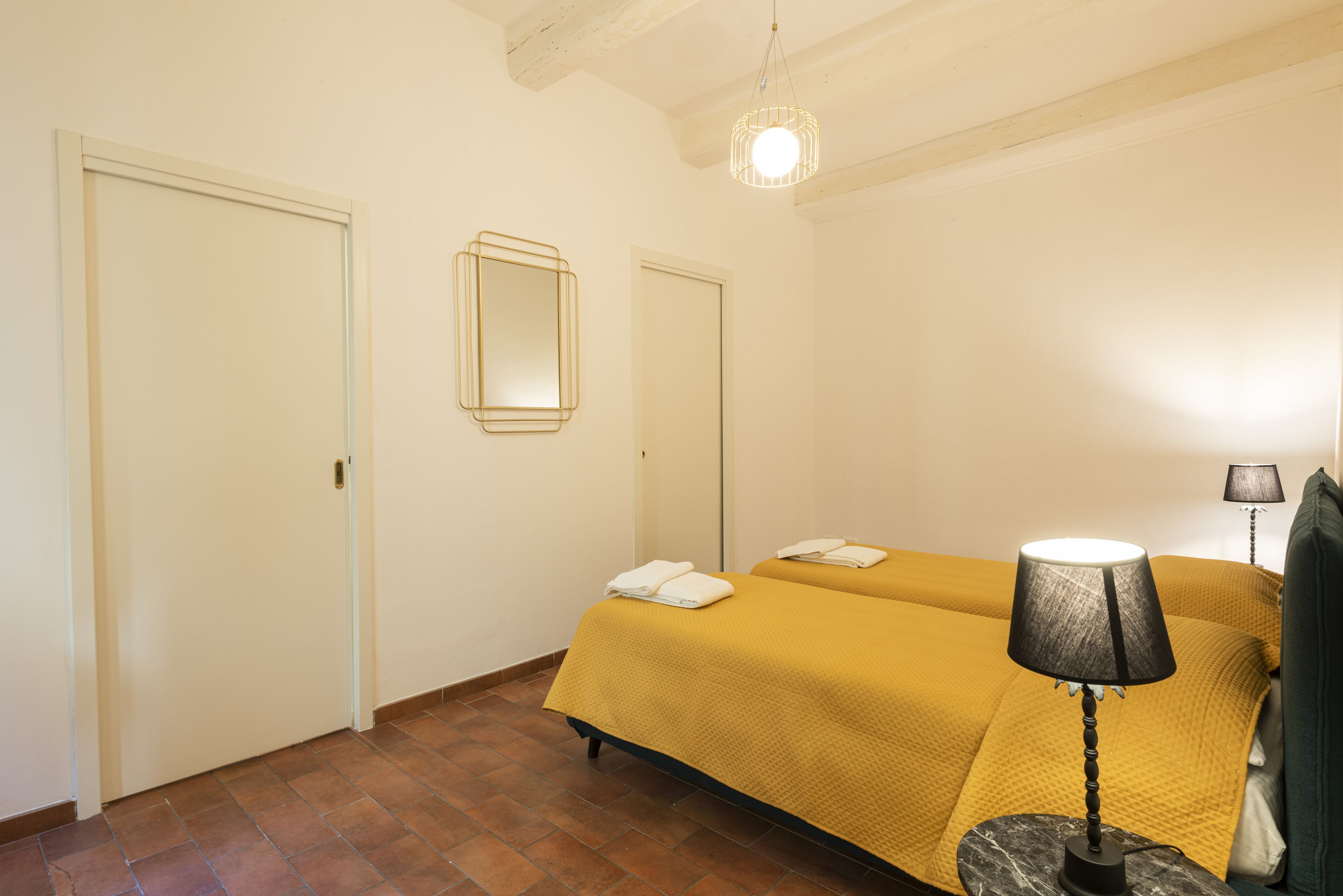 Una stanza con due letti, uno specchio, una lampada e una porta.