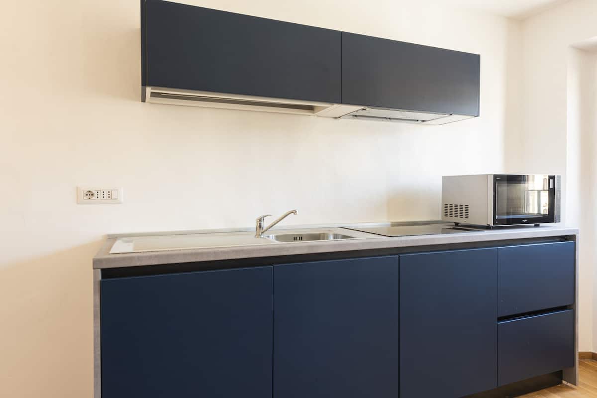 A kitchen with dark blue cabinets, a stainless steel sink, and a microwave.
