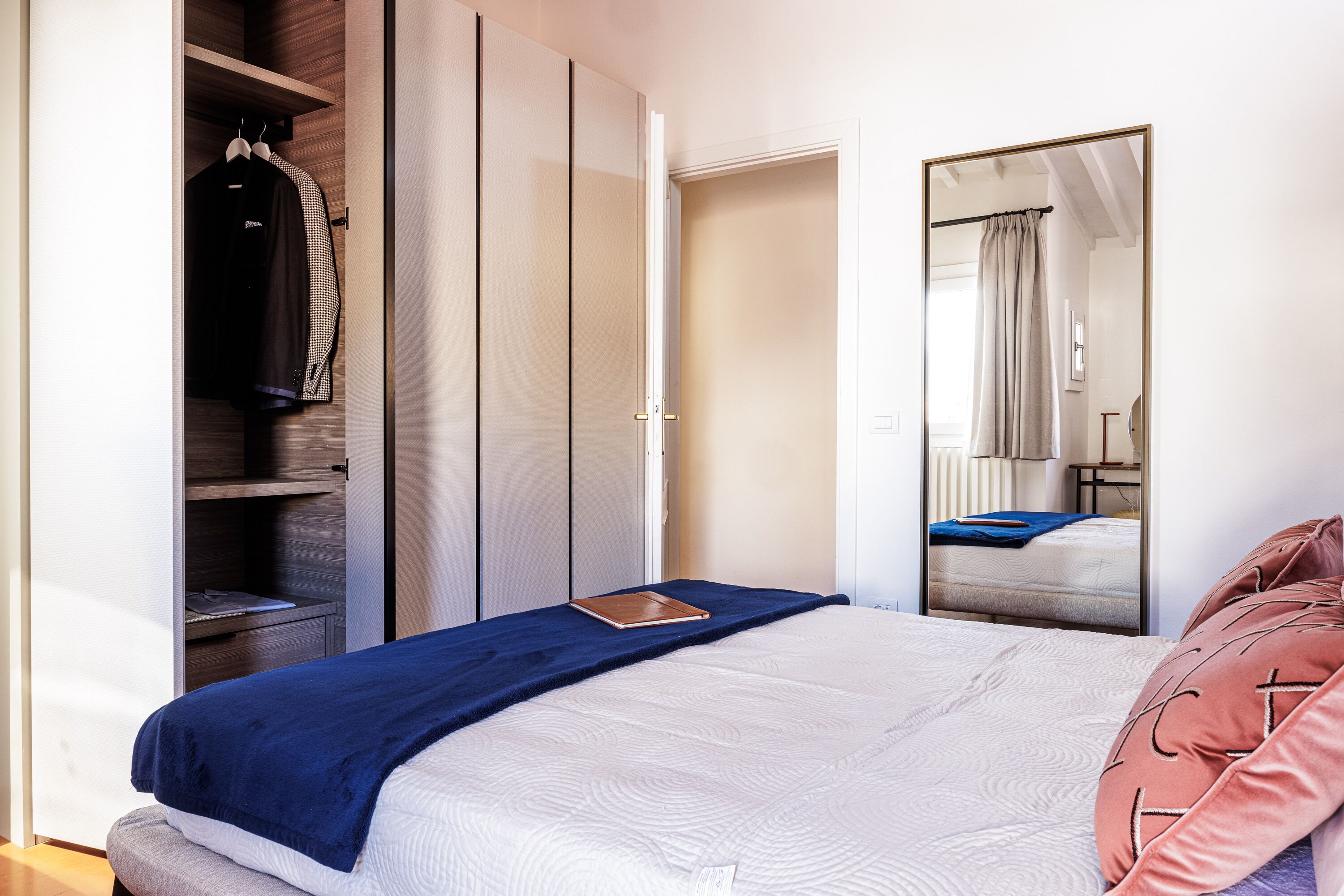 Quarto com cama, guarda-roupa, espelho e mesa de cabeceira.