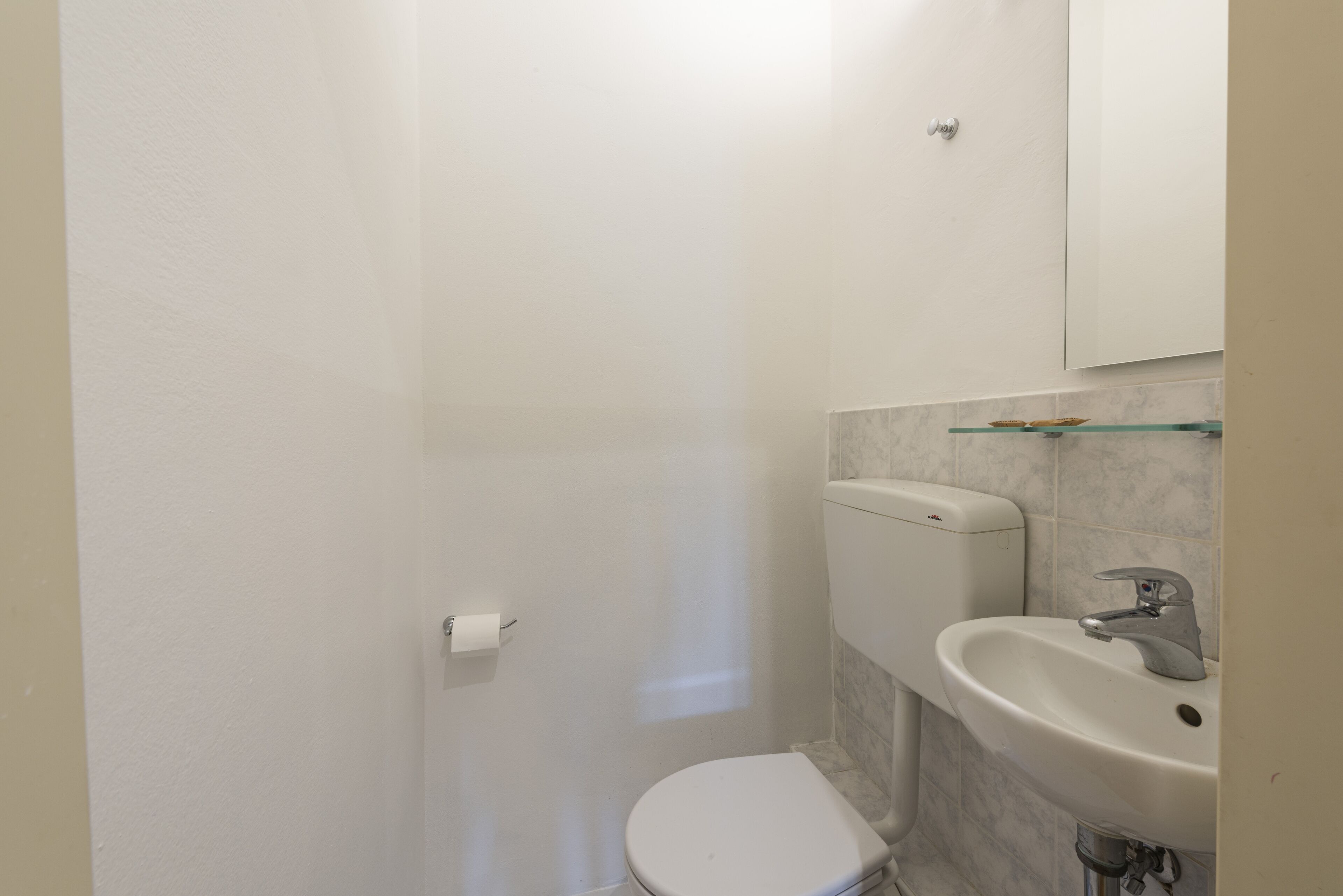 A small, white bathroom with a toilet, sink, and a mirror above the sink.
