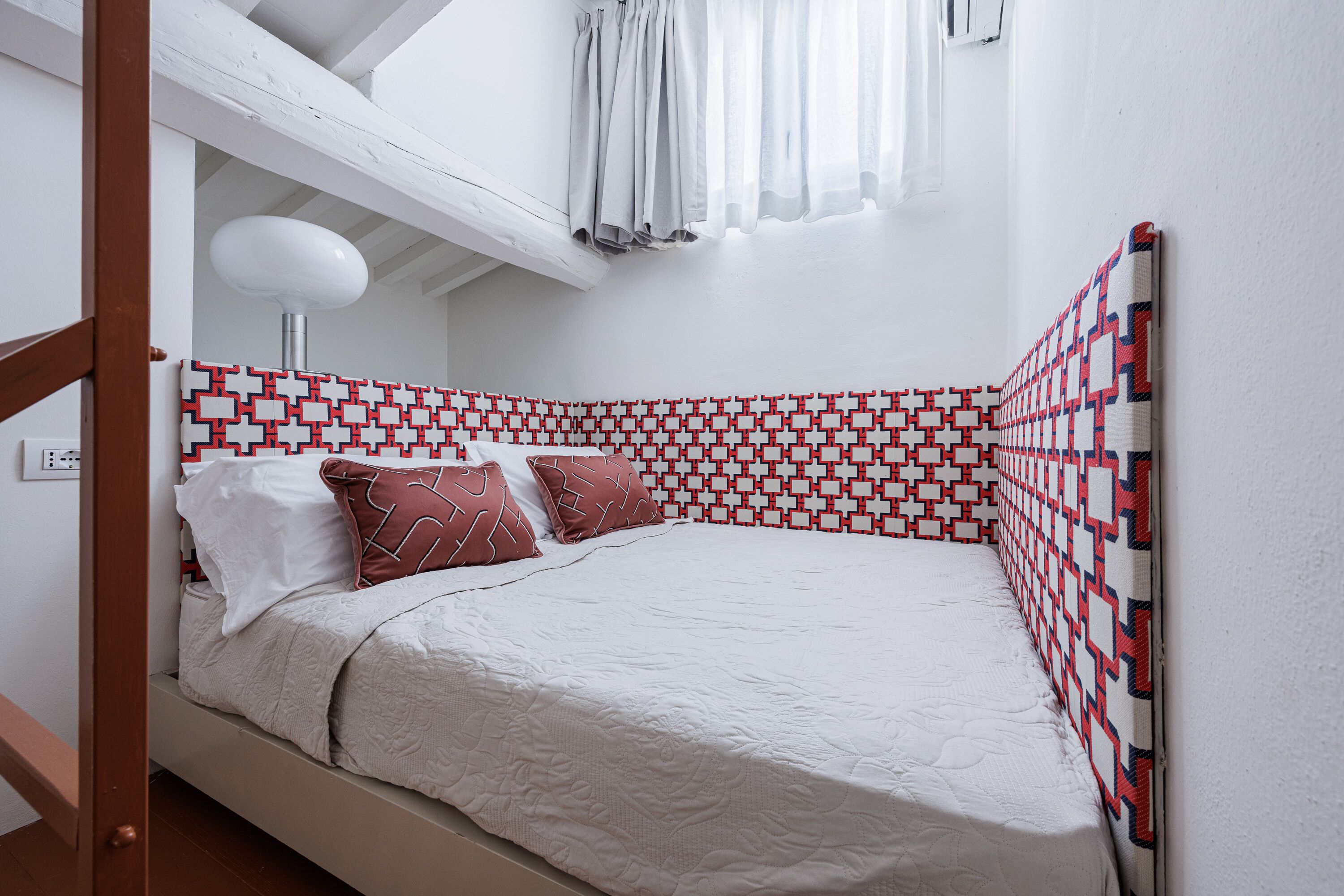 A bed with a patterned headboard, a bedside lamp, and a window with curtains.