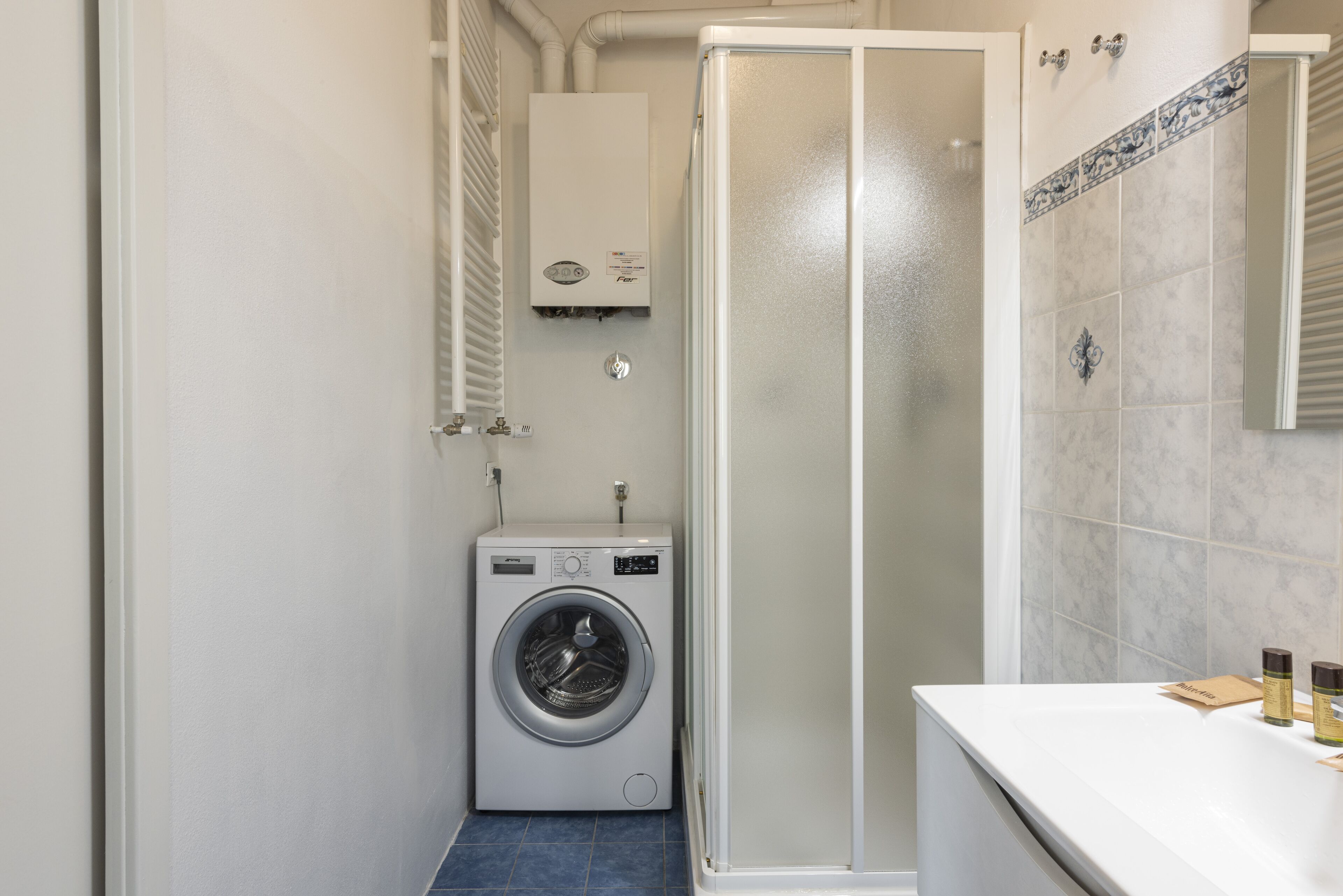 A compact bathroom with a washing machine, a glass shower enclosure, and a tiled wall.