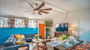 Ein Wohnzimmer mit Sofa, Couchtisch, Esstisch für zwei Personen und Fernseher.