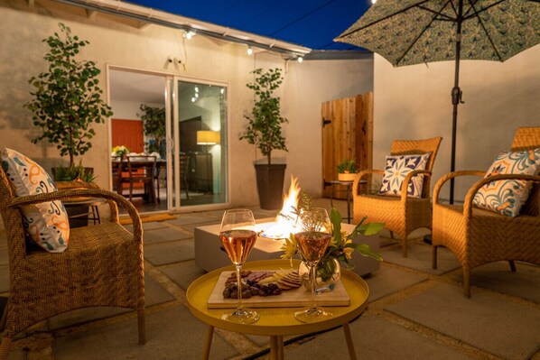 An outdoor patio area with wicker furniture, a table with a glass of wine, and a fire feature.