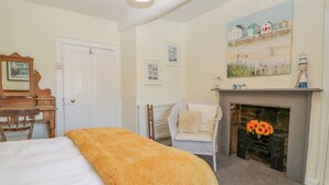 A bedroom with a bed, a chair, a fireplace, and a painting on the wall. - Bell Cottage (Dorchester)