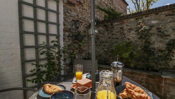 A breakfast setup with croissants, orange juice, and a pitcher on a table outside a building with stone walls. - Bell Cottage (Dorchester)