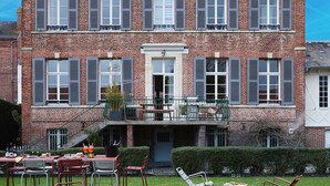 Un edificio de ladrillo de dos pisos con un balcón y un patio verde con mesas al aire libre.