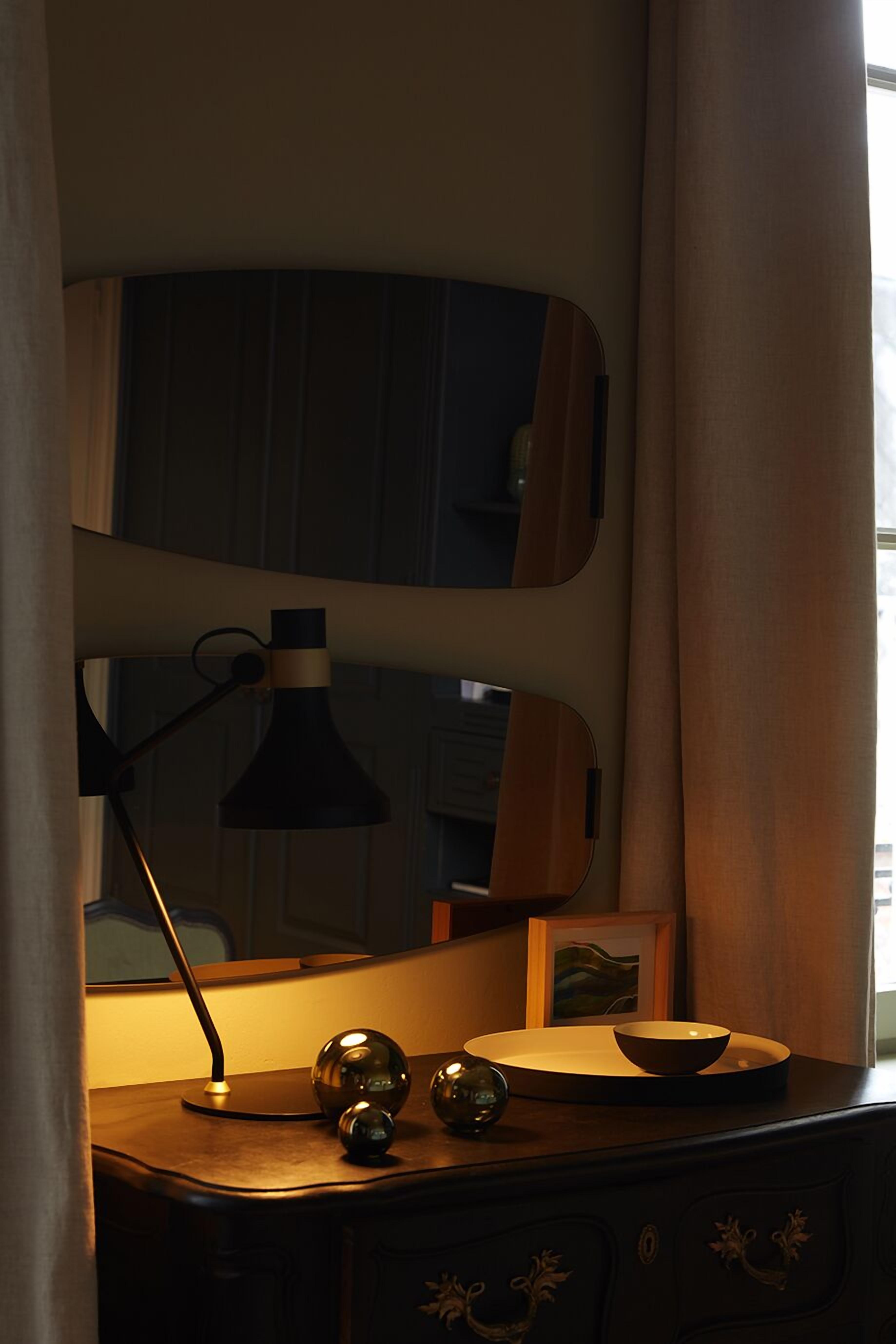 A desk with a lamp, a mirror, and decorative items.