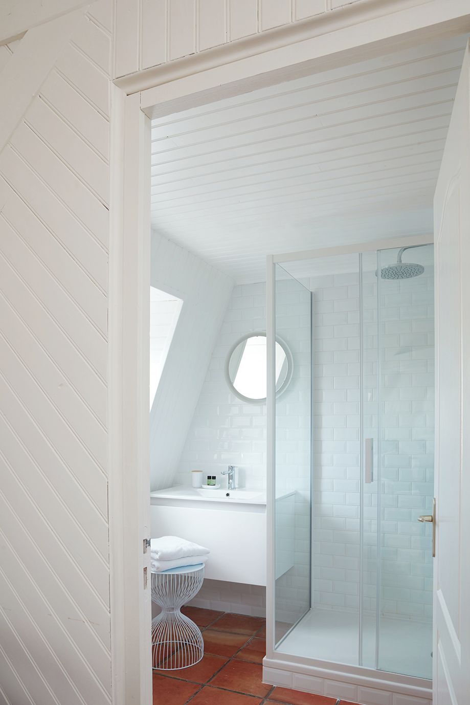 A modern bathroom with a glass-enclosed shower, a white sink with a round mirror, and a white toilet.