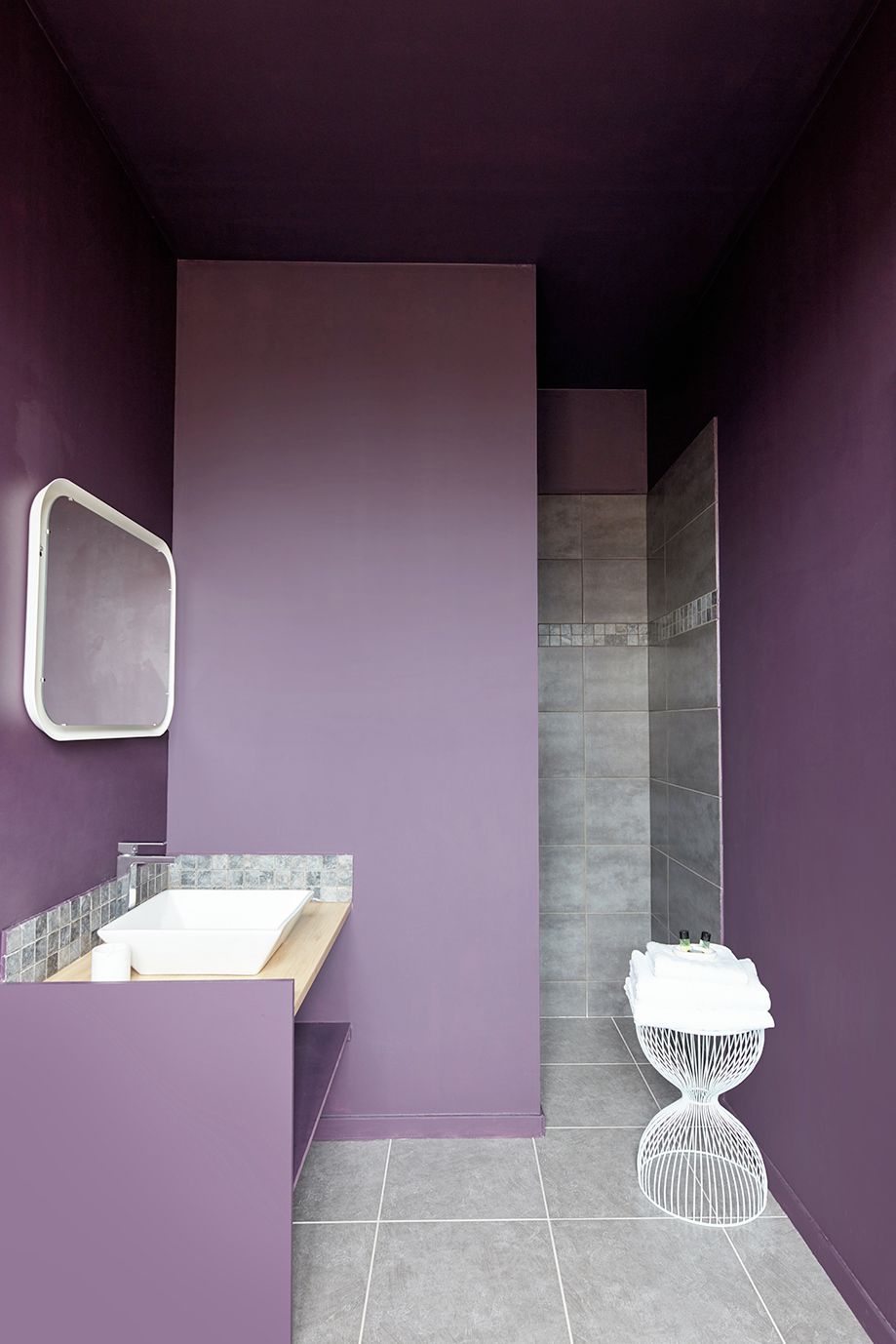 Een badkamer met een paarse wand, een wit wastafelmeubel en een douchegedeelte.