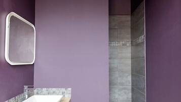 Een badkamer met een paarse wand, een wit wastafelmeubel en een douchegedeelte.