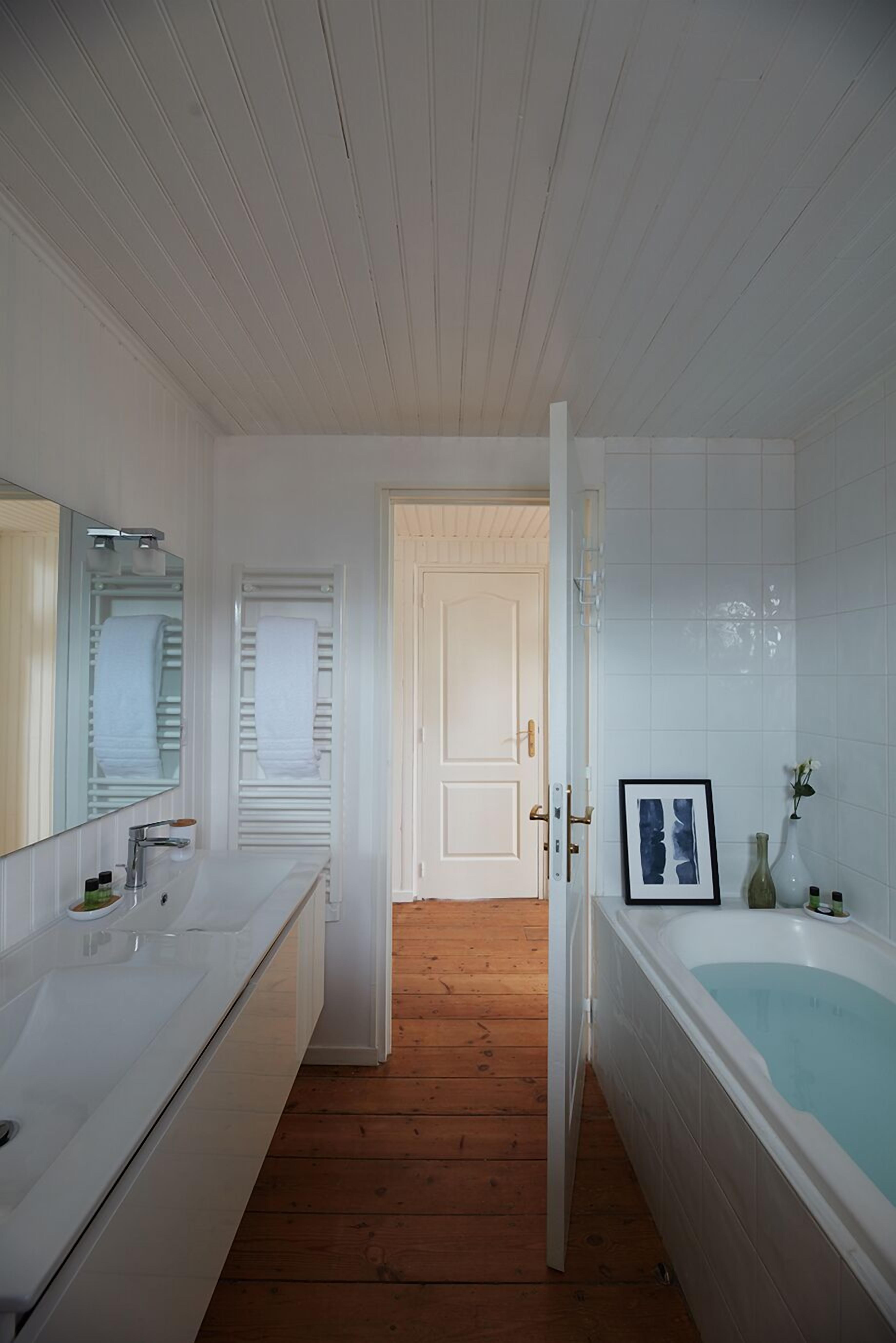 Een badkamer met een wit bad, een grote spiegel en een houten vloer.