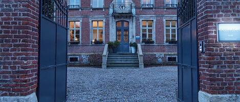 Een groot, historisch gebouw met een symmetrische gevel, een centrale ingang met treden en een bakstenen buitenkant.