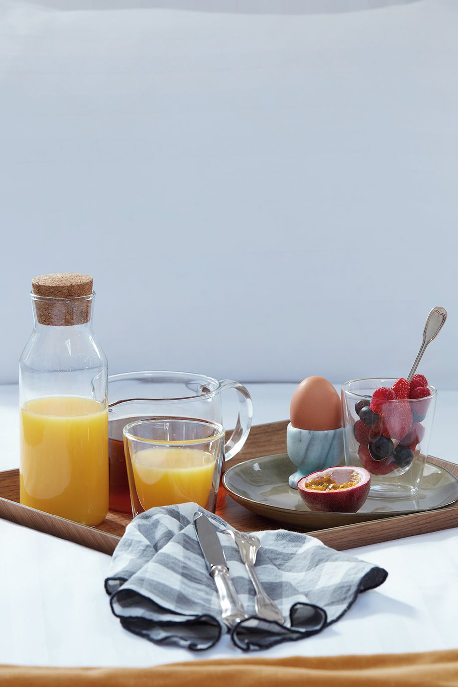 A breakfast setup with a bottle of orange juice, a glass of orange juice, a glass of milk, a plate with eggs, berries, and a spoon.