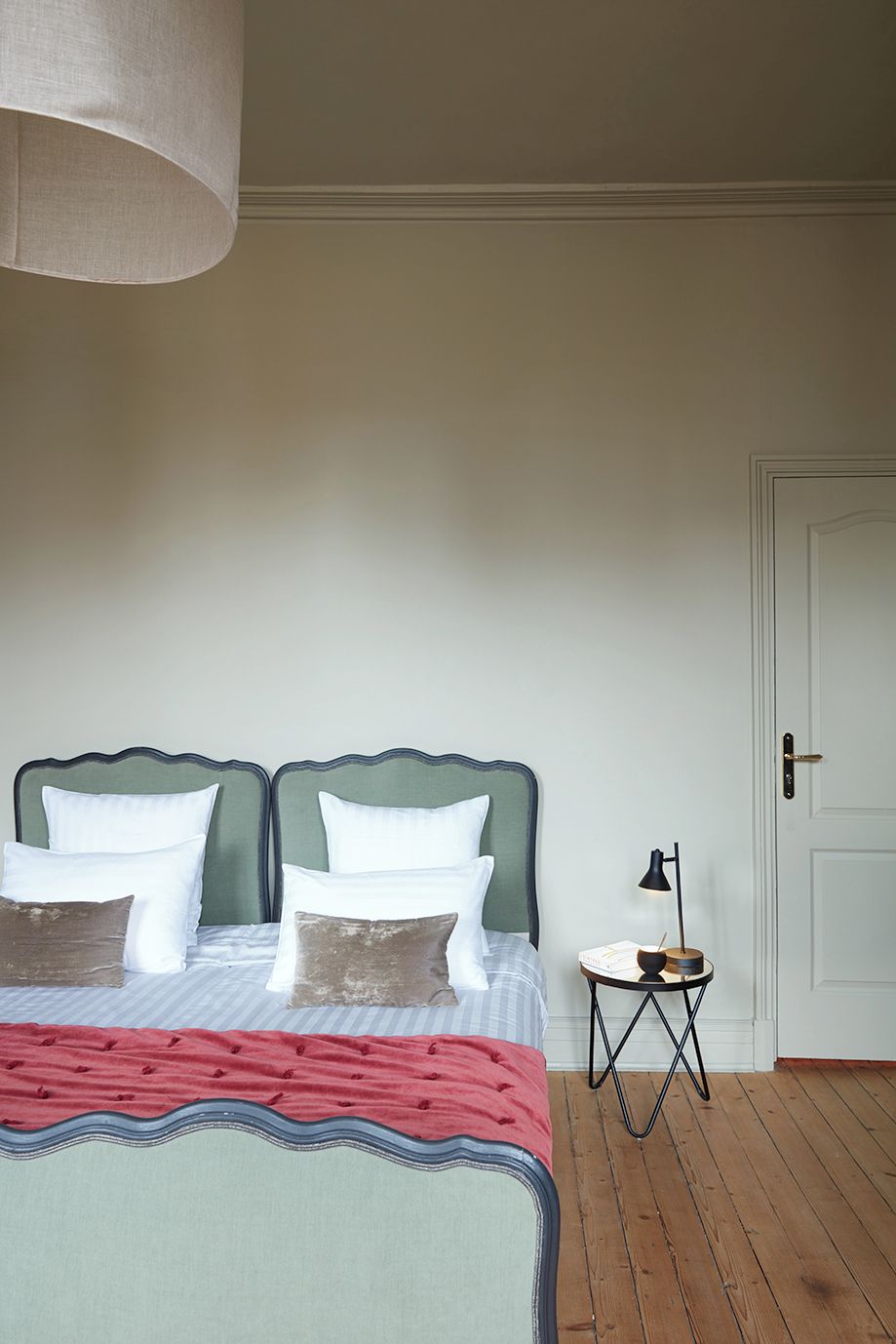Ein Schlafzimmer mit Bett, Kissen, einem Nachttisch mit Lampe und einer Tür.
