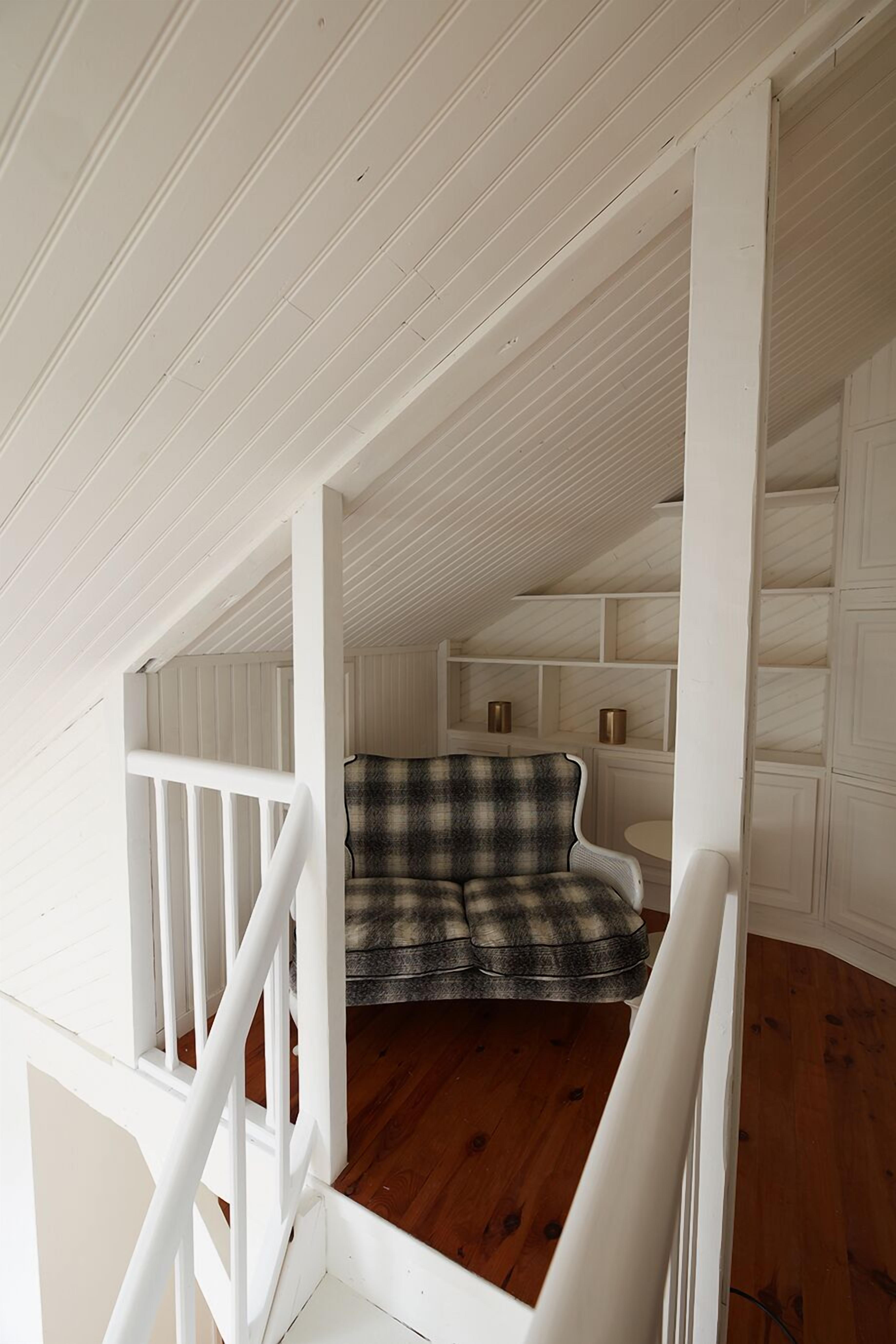Un escalier en bois mène à une chambre aménagée en mezzanine, où se trouvent un canapé à carreaux et des étagères intégrées.
