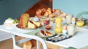 Una mesa de desayuno con diversas comidas y bebidas, incluyendo pan, bollería, frutas y una cafetera.