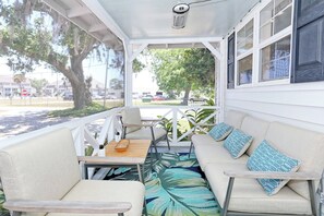 Un espacio de estar al aire libre techado con sofá y sillones, una mesa y vista a la calle.