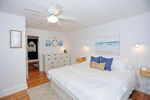 Un dormitorio con una cama grande, un ventilador de techo, una mesita de noche y una lámpara de pared.