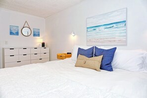 Une chambre à coucher avec un lit, une tête de lit blanche, des œuvres d’art murales et une table de chevet.