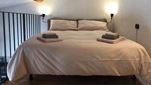 A bed with a beige comforter and pillows, two bedside lamps, and a wooden ceiling beam. - Sofia's Nest (Firenze)