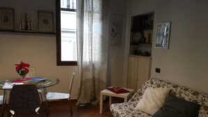 A living room with a round glass table, two chairs, a sofa, a small side table, and a patterned rug. - Sofia's Nest (Firenze)
