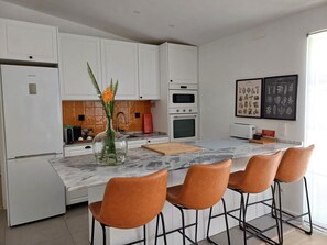 Une cuisine moderne avec des armoires blanches, un comptoir en marbre et quatre chaises marron.