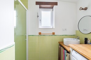 Une salle de bain avec un mur recouvert de carreaux verts, une fenêtre, un lavabo et un miroir.