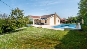 Ein Haus mit Swimmingpool, überdachter Terrasse und einem Garten mit weißen Blüten.