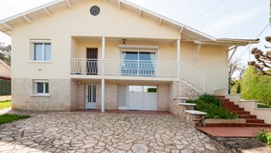 Ein zweistöckiges Haus mit einem aus Stein gepflasterten Eingangsbereich, einem Balkon mit weißen Geländern und einer Treppe, die zum Eingang führt.