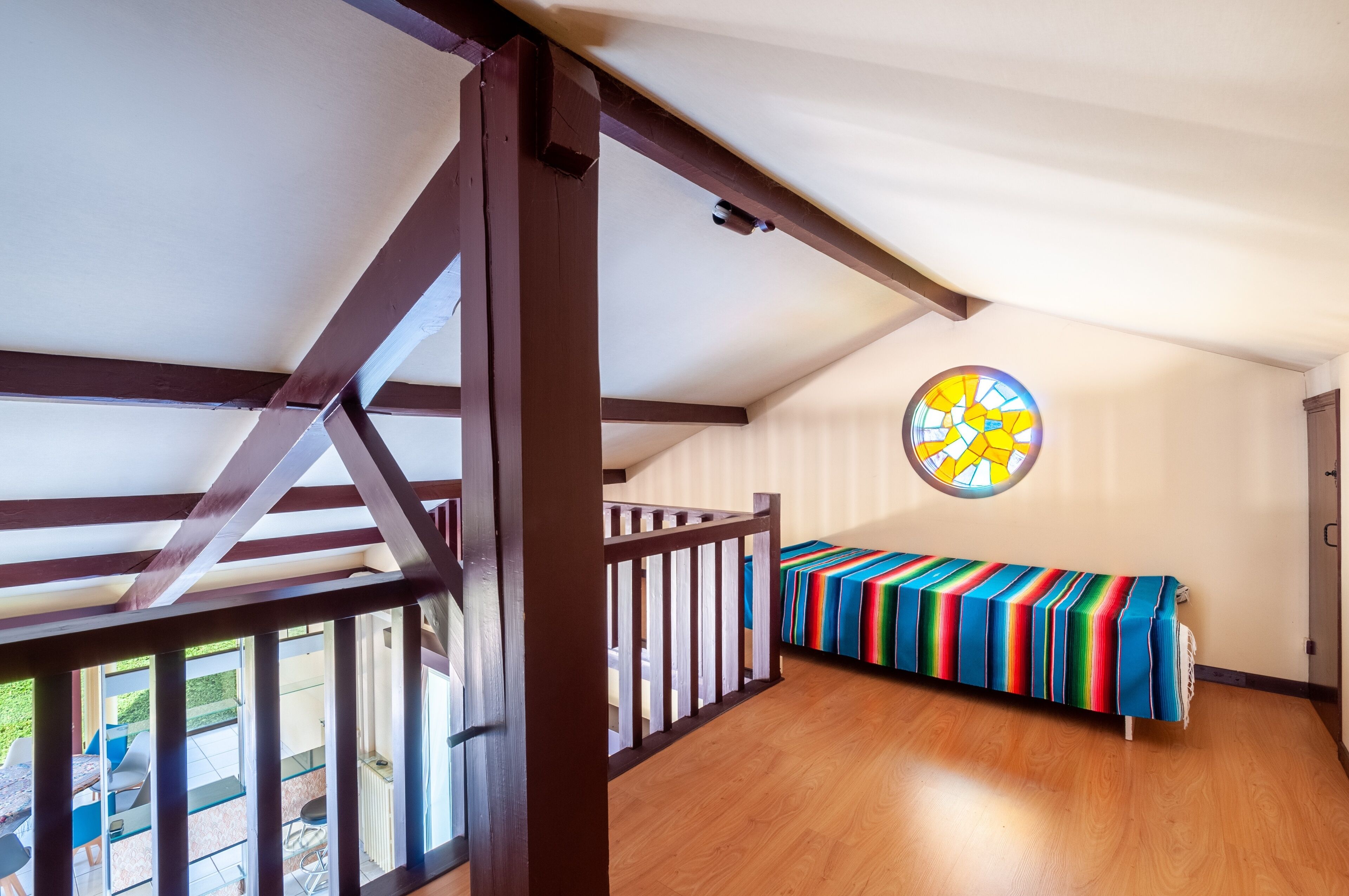 Una habitación con piso de madera, un banco colorido a rayas, un ventanal de vitral y vistas al exterior.