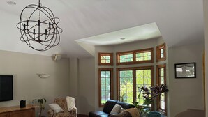 Un salon spacieux avec un plafond haut, de grandes fenêtres, un lustre et une table basse en bois.