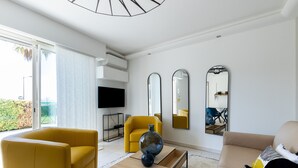 A modern living room with a yellow sofa, a beige sofa, and a coffee table with decorative vases. There are three large mirrors on the wall and a flat-screen TV mounted above the sofa. - Le Palm Beach - Jacuzzi et vue mer (Sanary-sur-Mer)