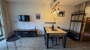 Ein Zimmer mit einem Holztisch, einem an der Wand befestigten Fernseher, einem Etagenbett und einer Pflanze auf dem Tisch.