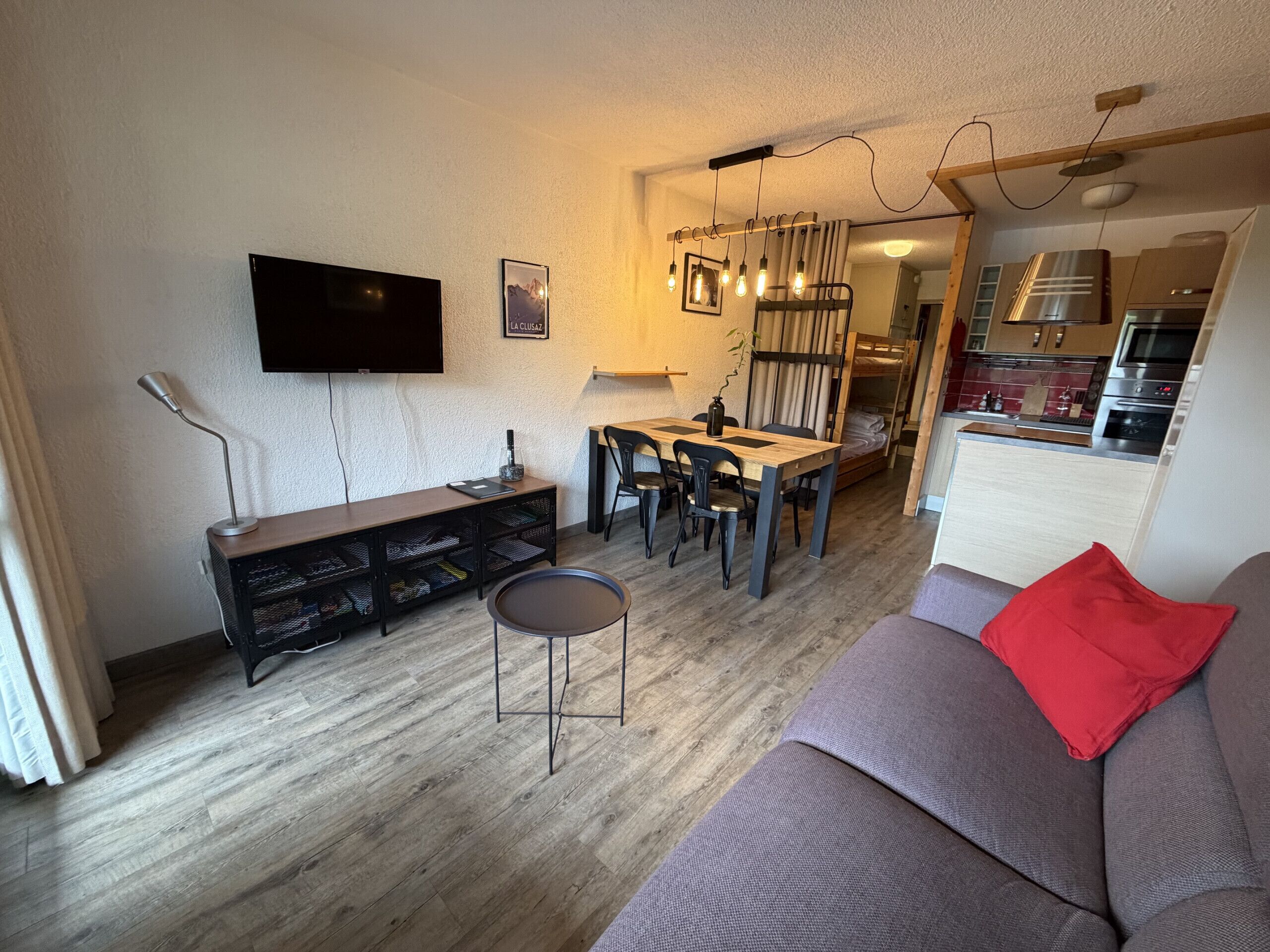 Ett kompakt bostadsutrymme med en matplats, en soffa, en tv och ett litet kök.