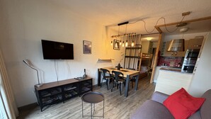 Ein kompakter Wohnbereich mit Essplatz, einer Couch, einem Fernseher und einer Küchenzeile.