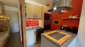 Eine kleine Küche mit Holzschränken, einem eingebauten Backofen, einer Mikrowelle und einer Kaffeemaschine.