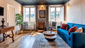 A cozy living room with a blue sofa, a wooden coffee table, a plant, and a view of the outdoors through large windows. - Genteel Home Piazza Pitti I (Florence)