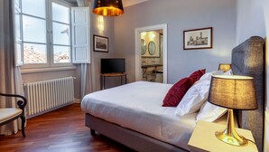 A bedroom with a bed, a TV, a lamp, a chair, and a window with curtains. - Genteel Home Piazza Pitti II (Florence)