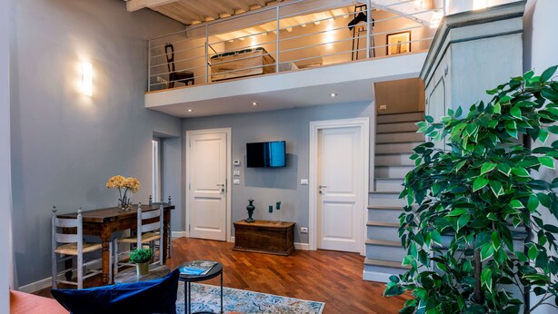 A spacious living area with a high ceiling, a wooden staircase, and a balcony. - Genteel Home Piazza Pitti II (Florence)