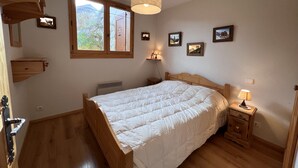 Un dormitorio con cama de madera, una ventana, una mesita de noche con lámpara y un estante en la pared.