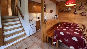 Una cocina compacta con armarios de madera, una mesa de comedor con mantel estampado y una escalera que lleva a otra habitación.