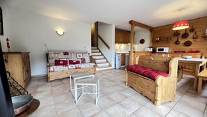 Una sala de estar acogedora con un sofá, un banco de madera, una mesita y una escalera que lleva a una cocina.