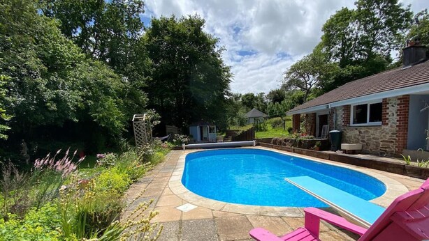 A swimming pool with a stone deck, surrounded by lush greenery and a pink chair. - Family Home With Large Garden and Pool Near Totnes (Totnes)