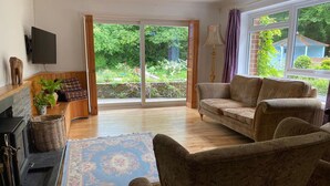 A living room with a fireplace, a sofa set, a large window with a view of greenery, and a lamp. - Family Home With Large Garden and Pool Near Totnes (Totnes)
